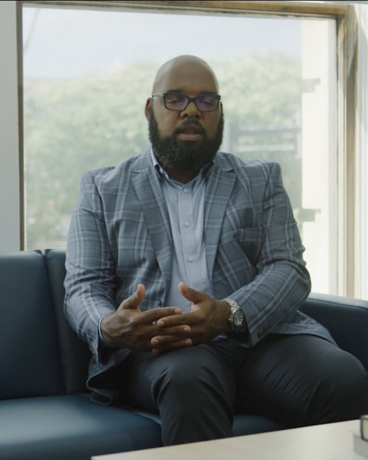 Interview subject on a sofa in front of large office windows